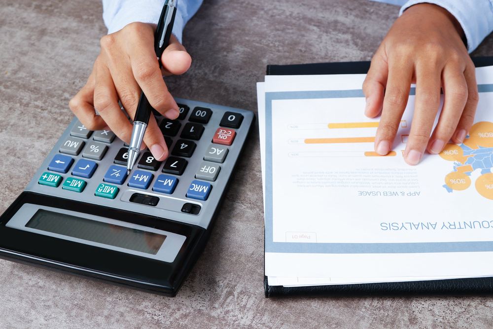 Hands using a calculator beside a printed business chart