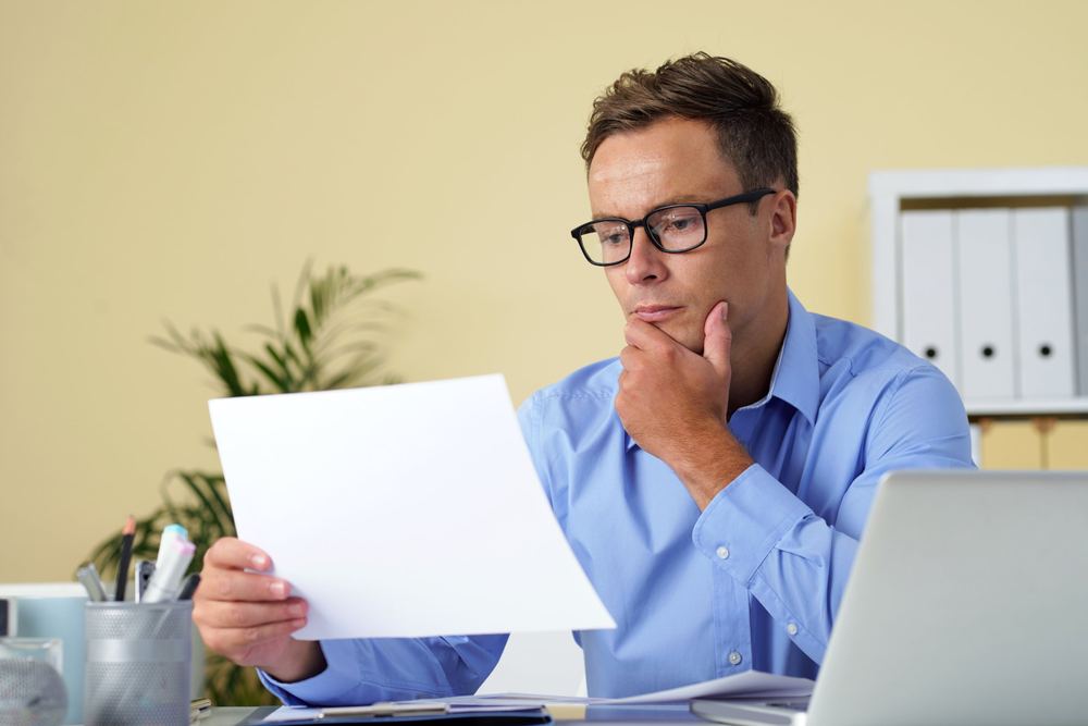 A man in glasses reading a document at his desk