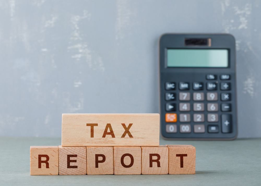 Wooden blocks spelling TAX REPORT beside a calculator
