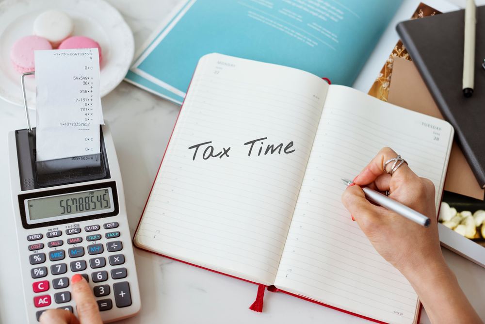 A hand writing Tax Time in a planner beside an adding machine